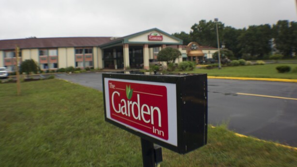 A Garden Inn sign in front of a building with a red roof and beige walls.