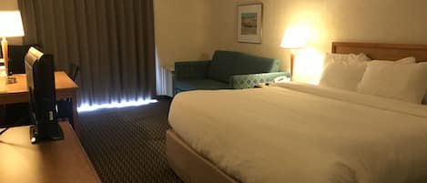 Una habitación de hotel con una cama grande, un escritorio con computadora, una silla, un sofá y una lámpara.