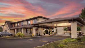 Um motel com área de estacionamento coberta, um carro estacionado na frente e um céu ao pôr do sol.