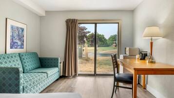 A hotel room with a bed, a sofa, a dining table with a chair, a lamp, and a large window with a view of the outdoors.
