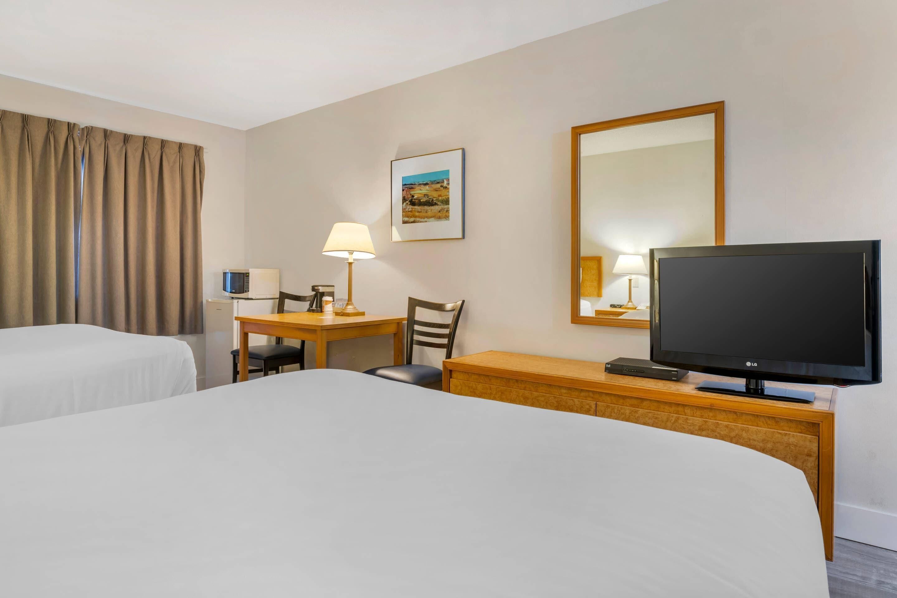 A hotel room with two beds, a desk with a lamp, a television, and a picture on the wall.