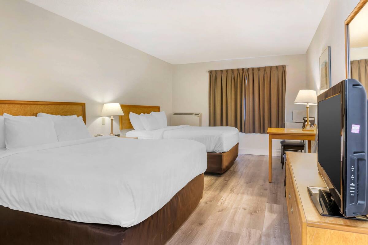 A hotel room with two beds, a desk with a television, and a window with curtains.