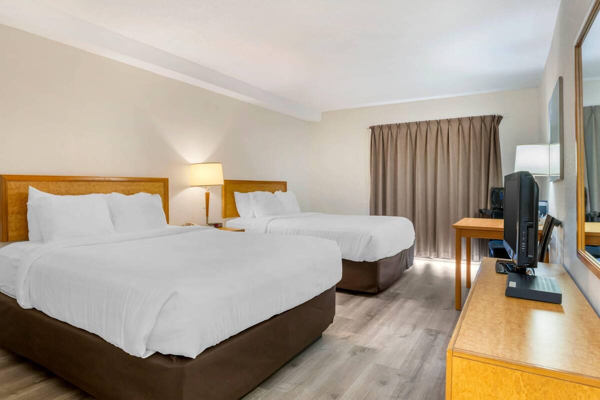 A hotel room with two beds, a desk with a computer, and a large mirror.