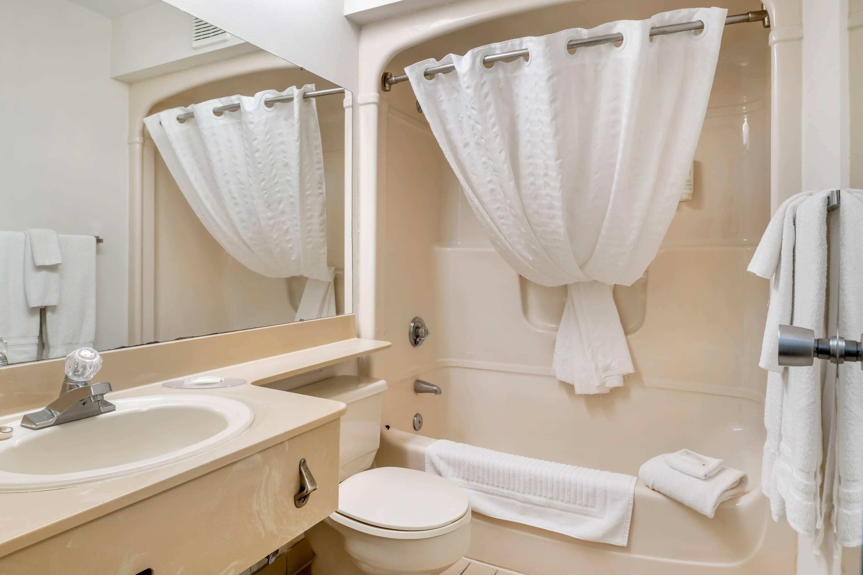 Et badeværelse med vask, toilet, badekar og et spejl.