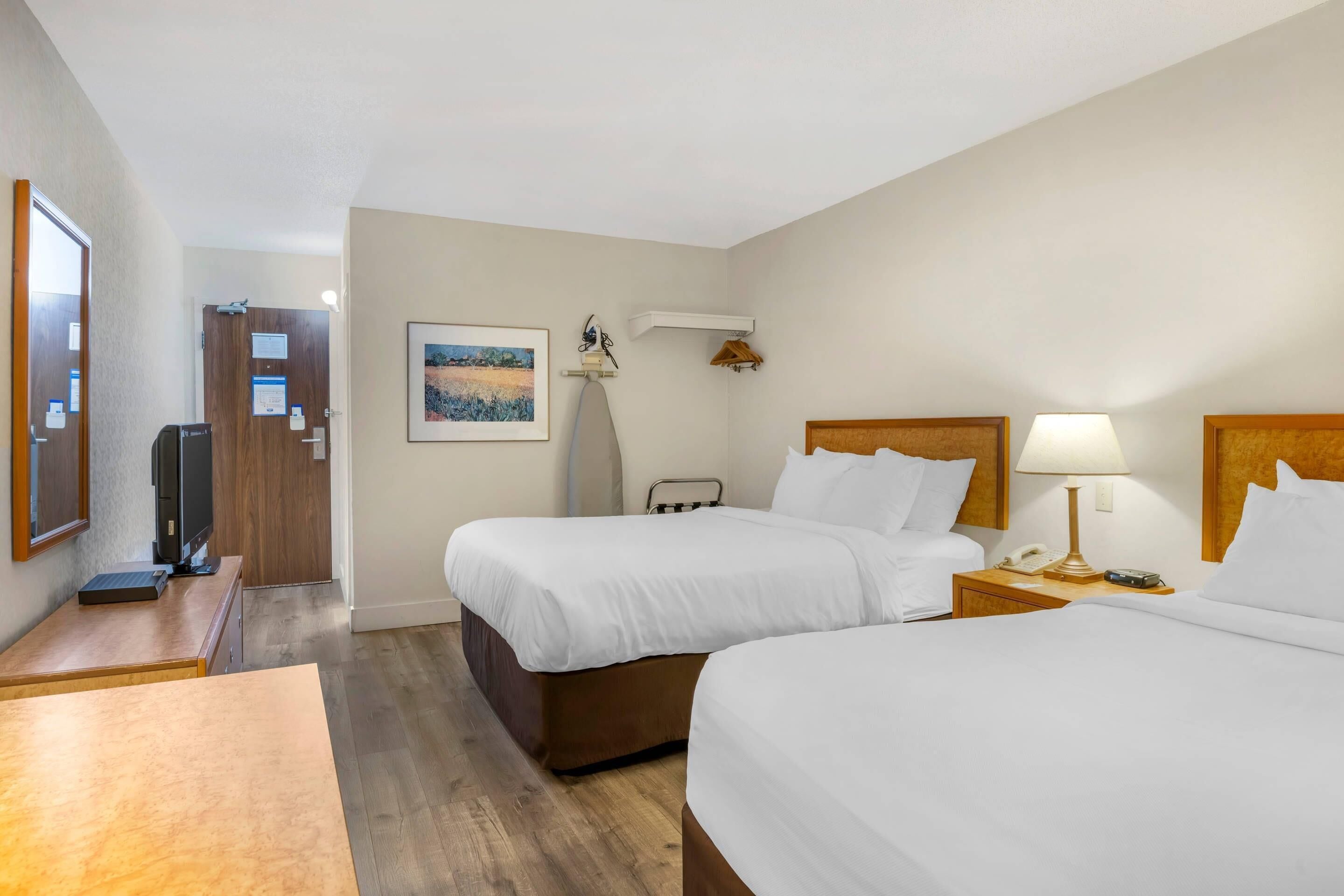 A hotel room with two beds, a desk, a television, a lamp, and a painting on the wall.