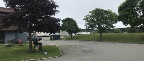 A parking lot with a grassy area, a bench, and a building with a garage door.