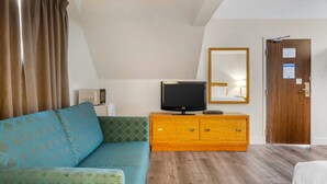 Quarto com sofá, televisão sobre um armário de madeira, porta de madeira e espelho na parede.
