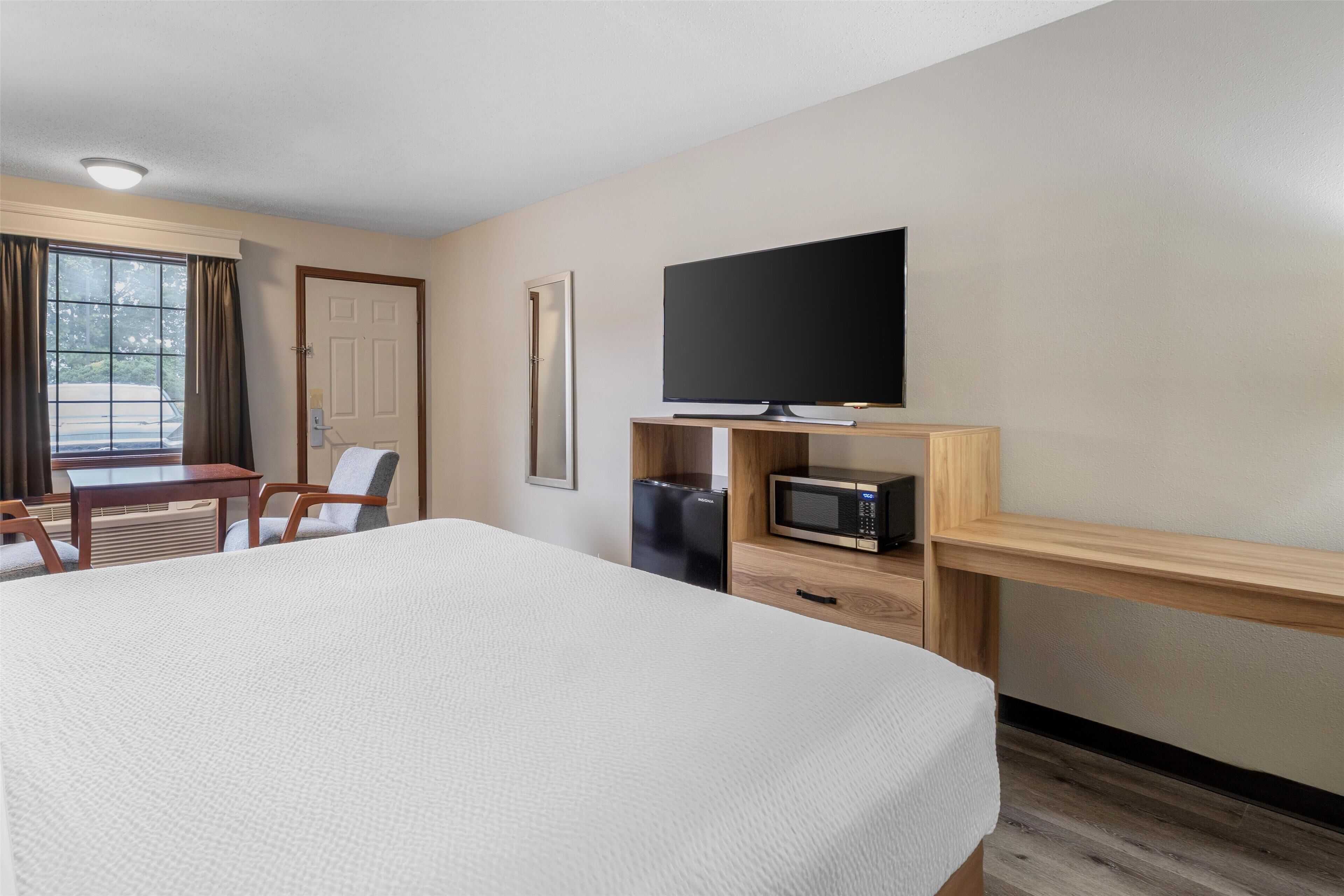 Habitación de hotel con una cama grande, un escritorio con silla, televisión, microondas y refrigerador.