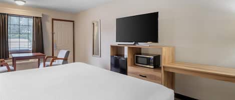 Habitación de hotel con una cama grande, un escritorio con silla, televisión, microondas y refrigerador.