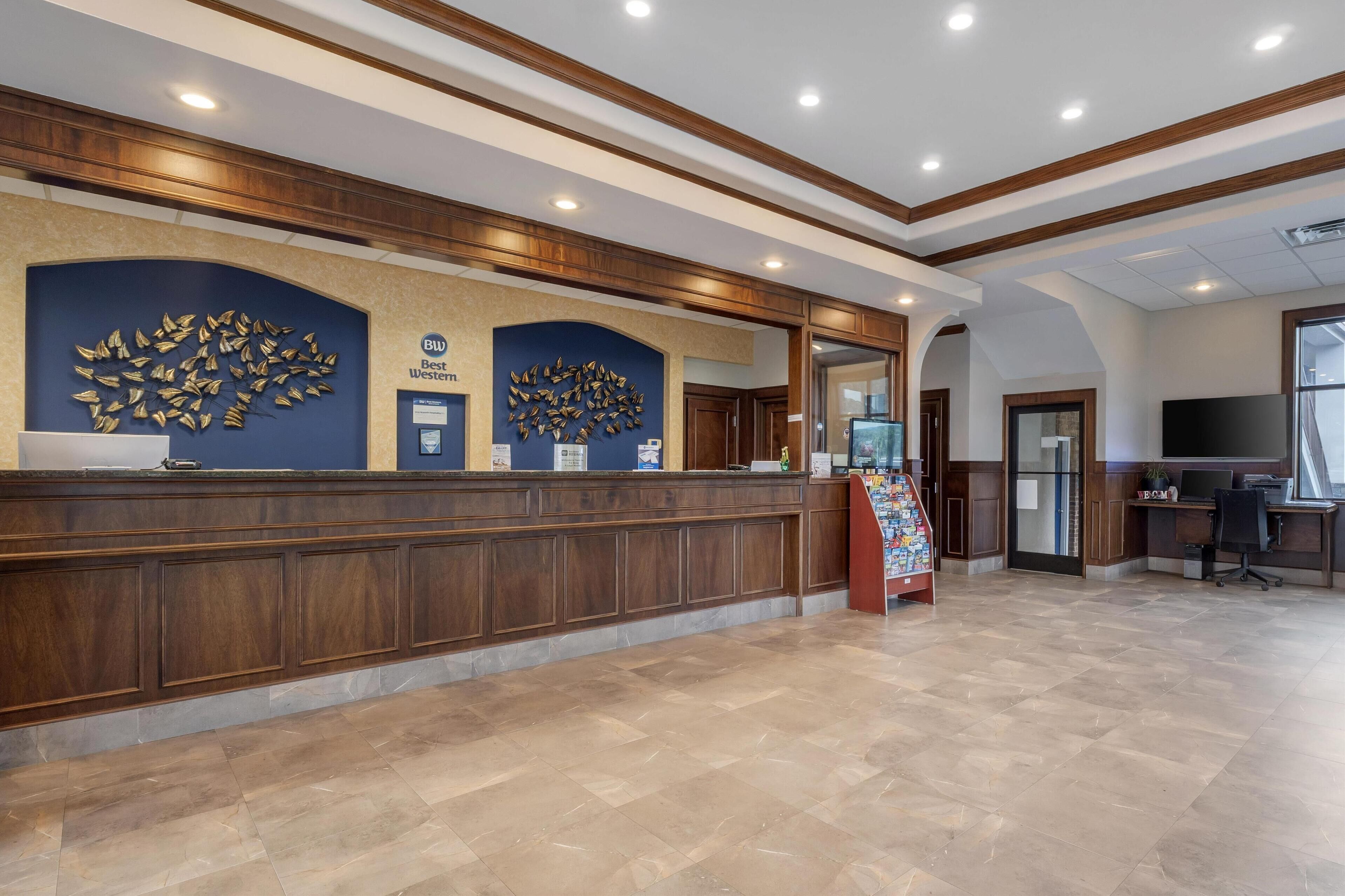 A reception area with a wooden reception desk, two wall-mounted information boards, and a tiled floor.