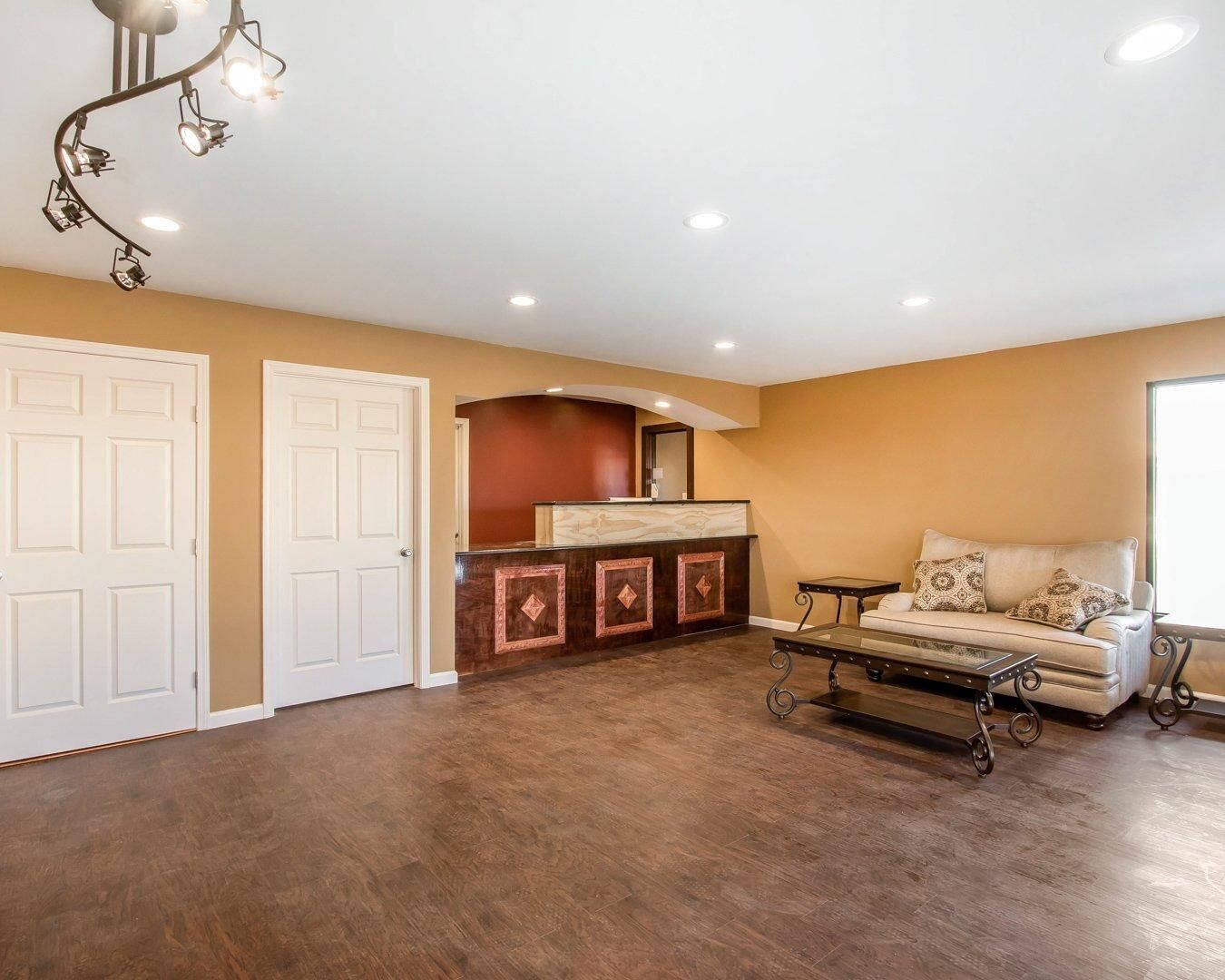 A spacious room with a wooden floor, a sofa, a small table, and a reception desk with a mirror.