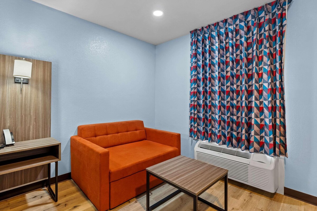 A room with a sofa, a small table, a wall-mounted lamp, and a patterned curtain.