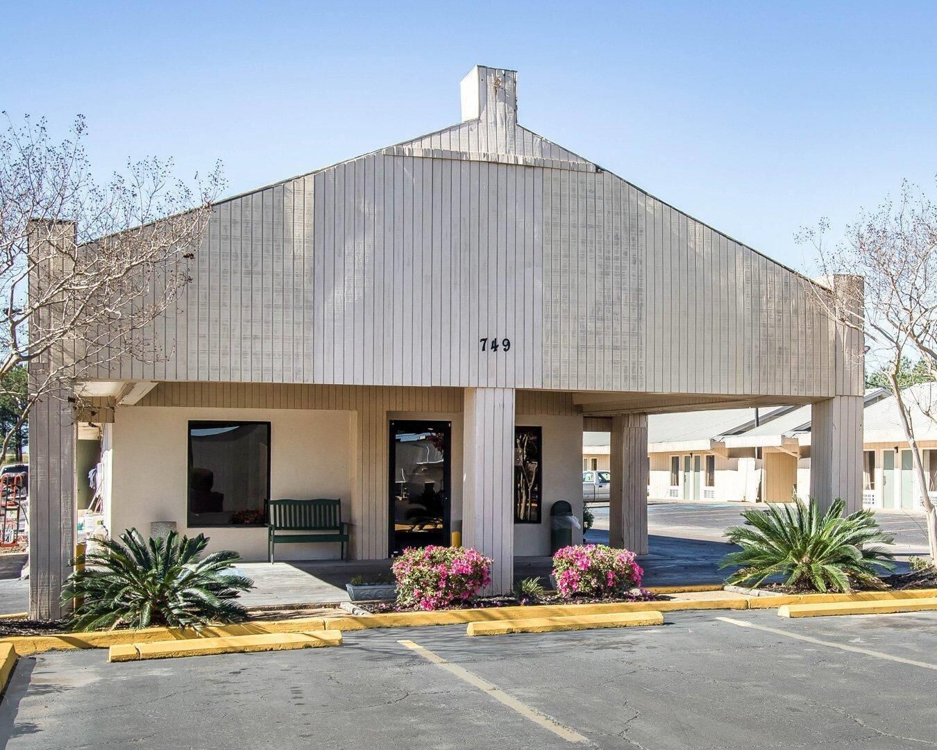 A building with a flat roof, a visible address number, and a covered entrance area with a bench and potted plants.