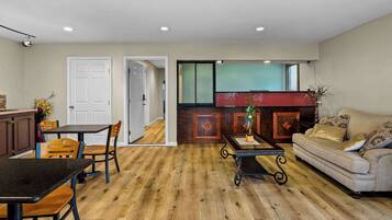 A spacious living area with a wooden floor, a sofa, a dining table with chairs, and a kitchen area with cabinets and a countertop.