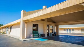 A motel with a covered parking area, a green bench, and a trash can.