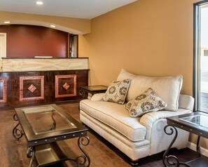 A hotel lobby with a sofa, two side tables, a glass-top coffee table, and a reception desk with a wooden panel design. - Rodeway Inn & Suites Brookhaven (Brookhaven)