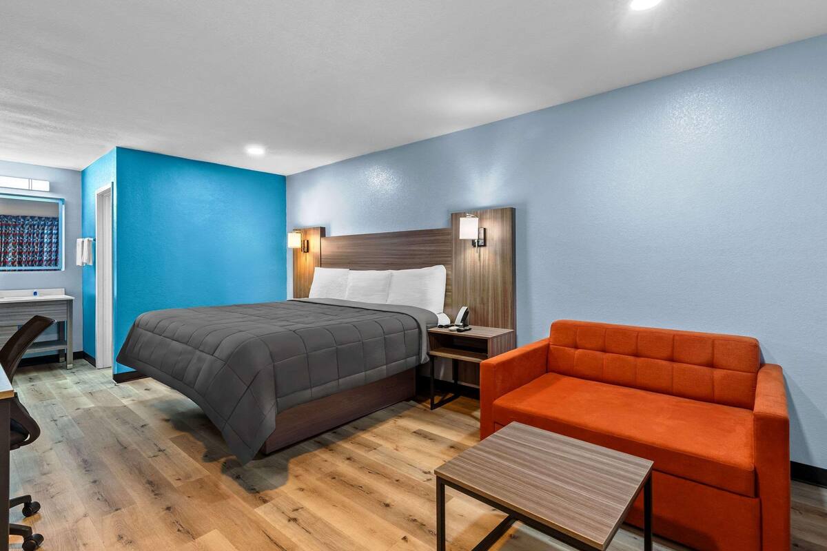 Quarto de hotel com cama, escrivaninha, cadeira e mesa de cabeceira.