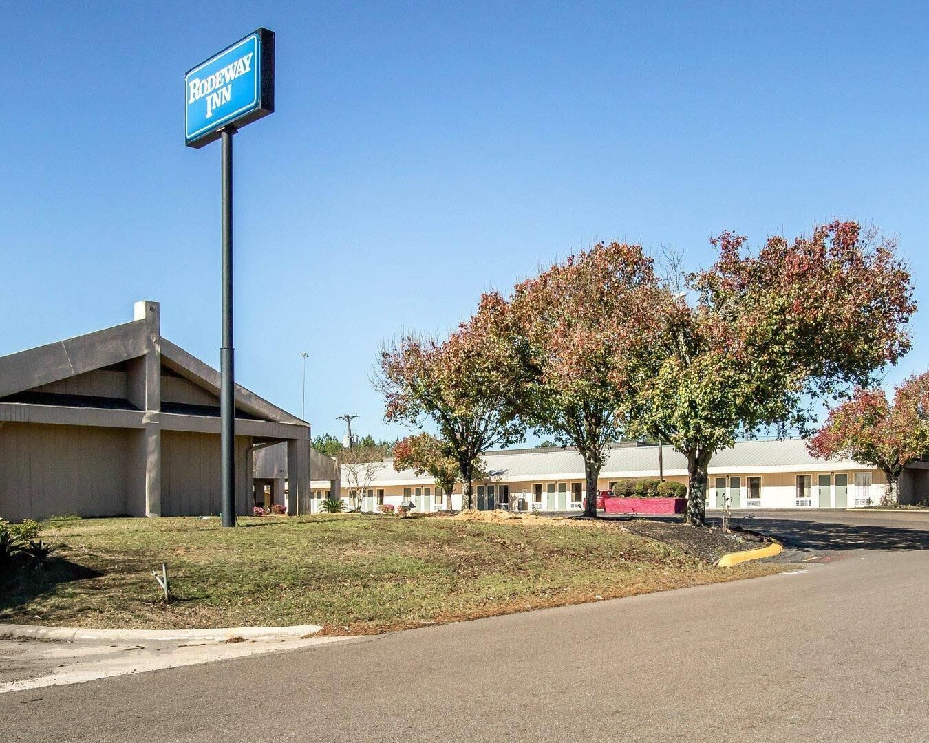 A motel named 'Rodeway Inn' with a clear sky, a parking lot, and a building with a sloped roof.
