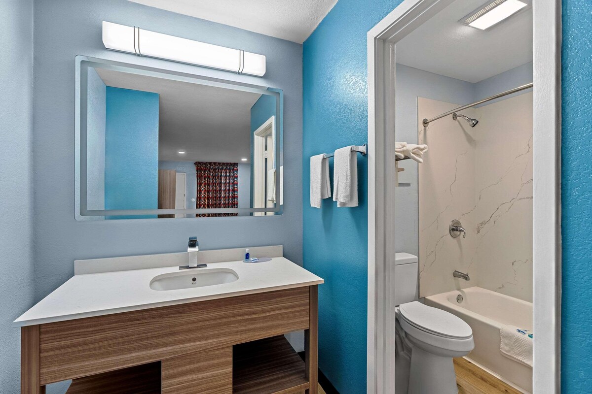 A bathroom with a white sink, mirror, and toilet, a shower with a glass door, and blue walls.