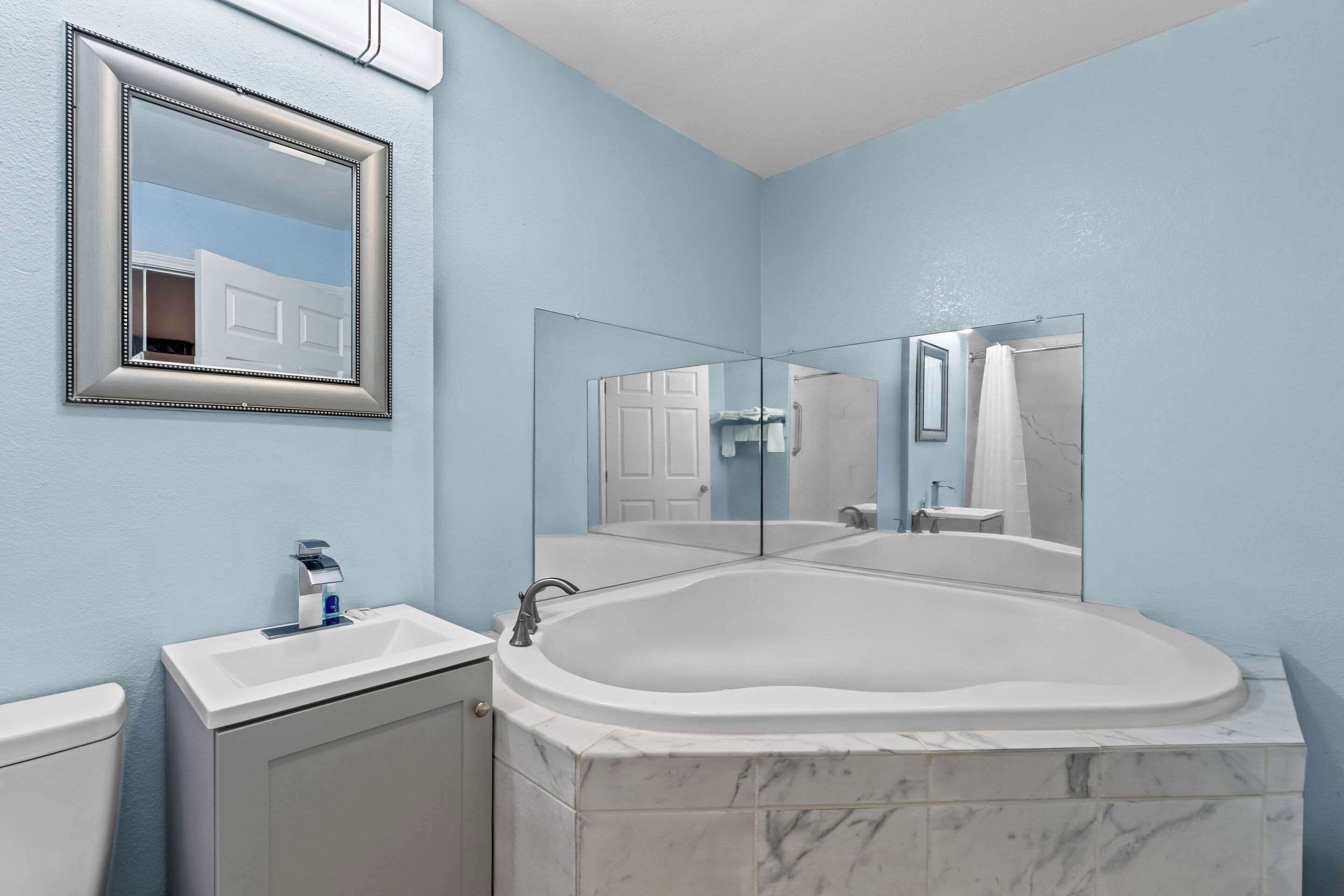 A bathroom with a marble bathtub, a sink, a toilet, and a mirror.