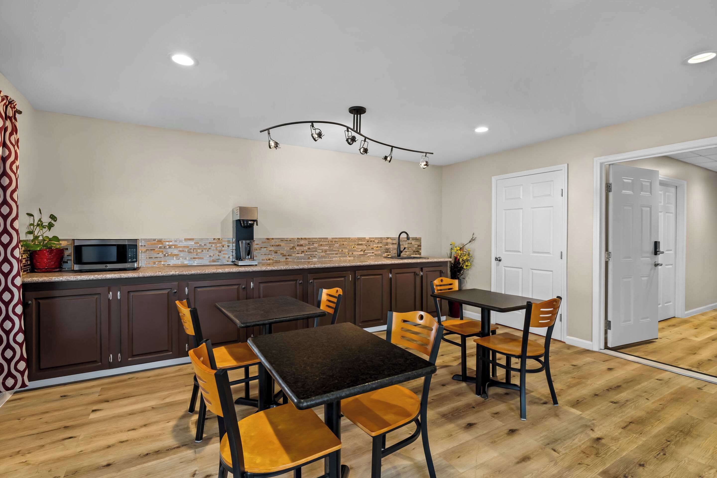 A modern kitchen with dark cabinets, a central island, and a dining area with wooden chairs.