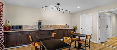 A modern kitchen with dark cabinets, a central island, and a dining area with wooden chairs.