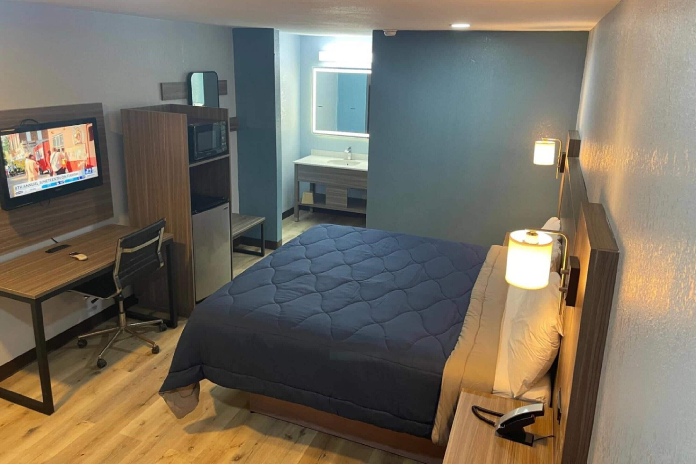 A hotel room with a bed, a desk with a computer, a television, a wardrobe, and a bathroom.