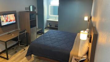 A hotel room with a bed, a desk with a computer, a television, a wardrobe, and a bathroom.