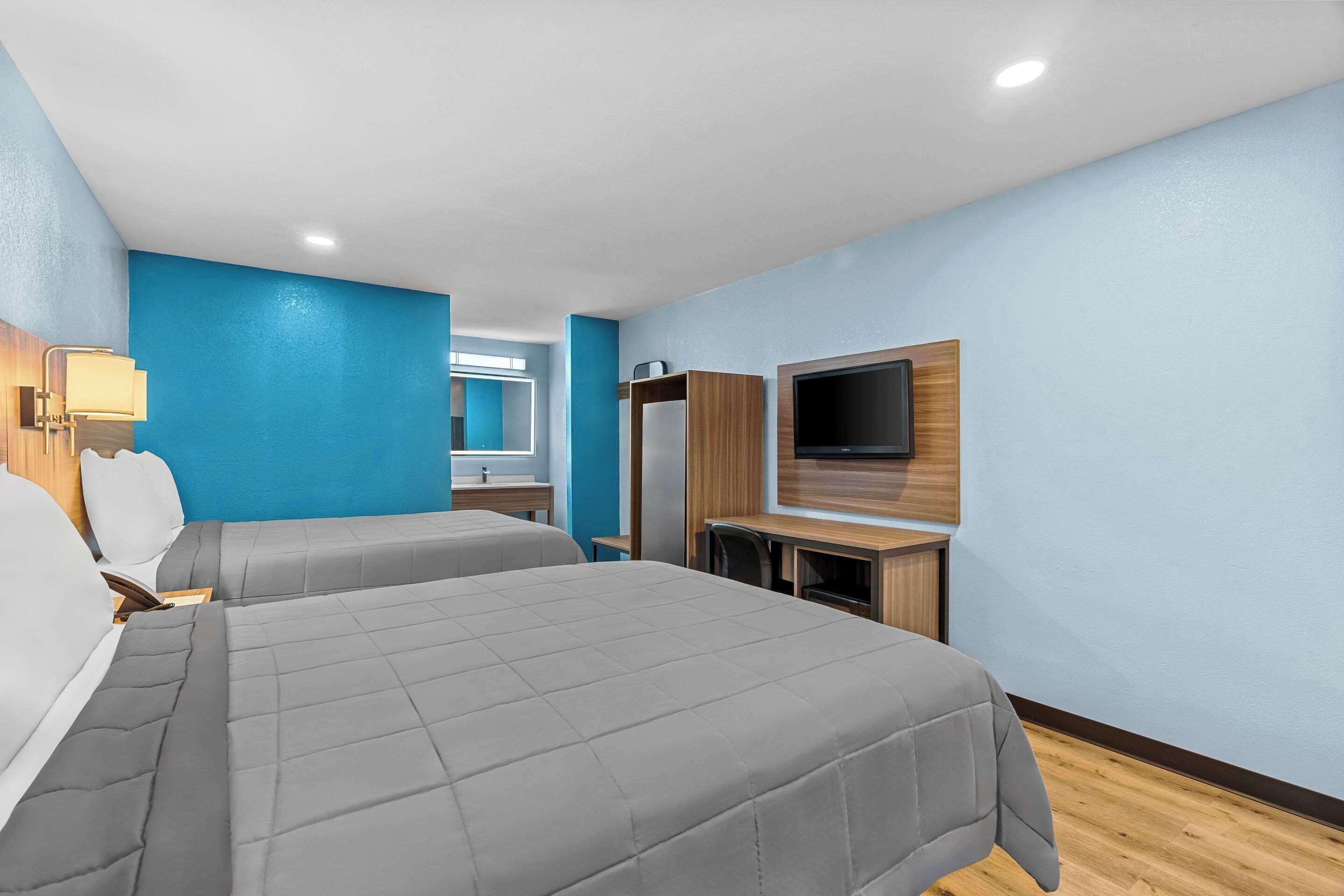 A hotel room with two beds, a TV, a desk, and a mirror.