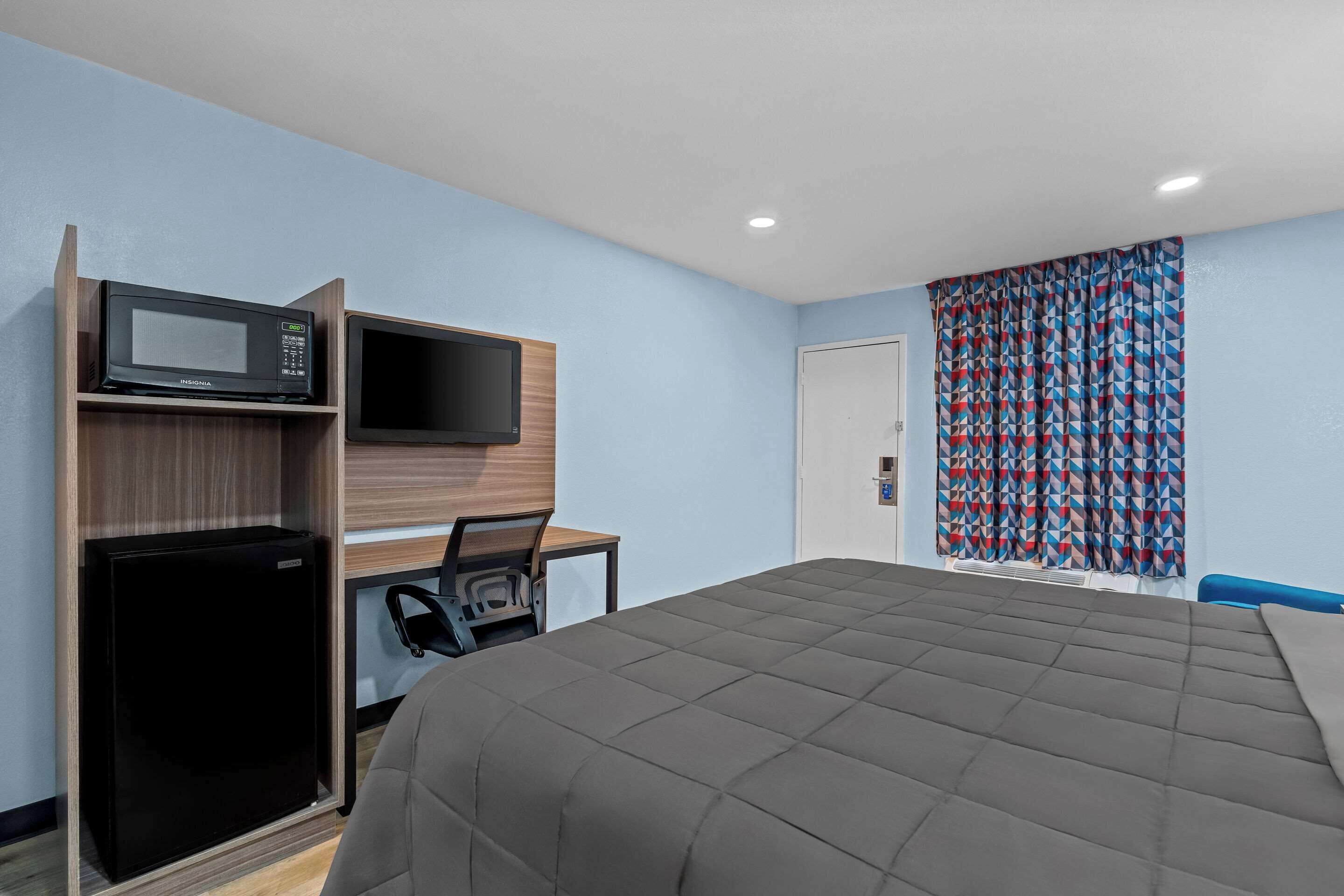 A hotel room with a bed, a desk with a computer, a microwave, and a refrigerator.