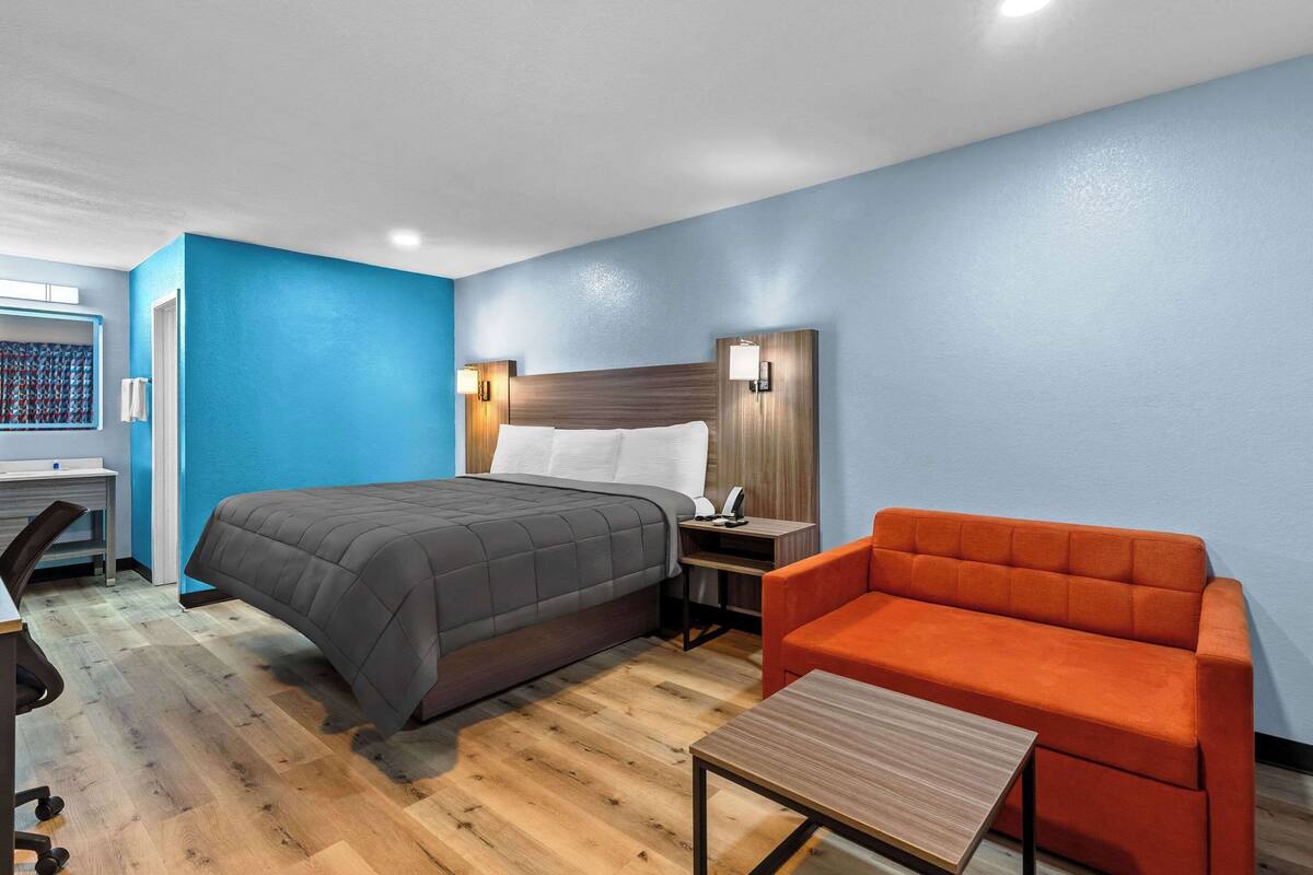 Quarto de hotel com cama, escrivaninha, cadeira e mesa de cabeceira com abajur.
