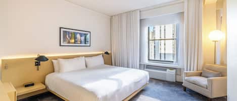 Una habitación de hotel con una cama grande, una silla, una ventana con cortinas, una lámpara de pared y un cuadro enmarcado.