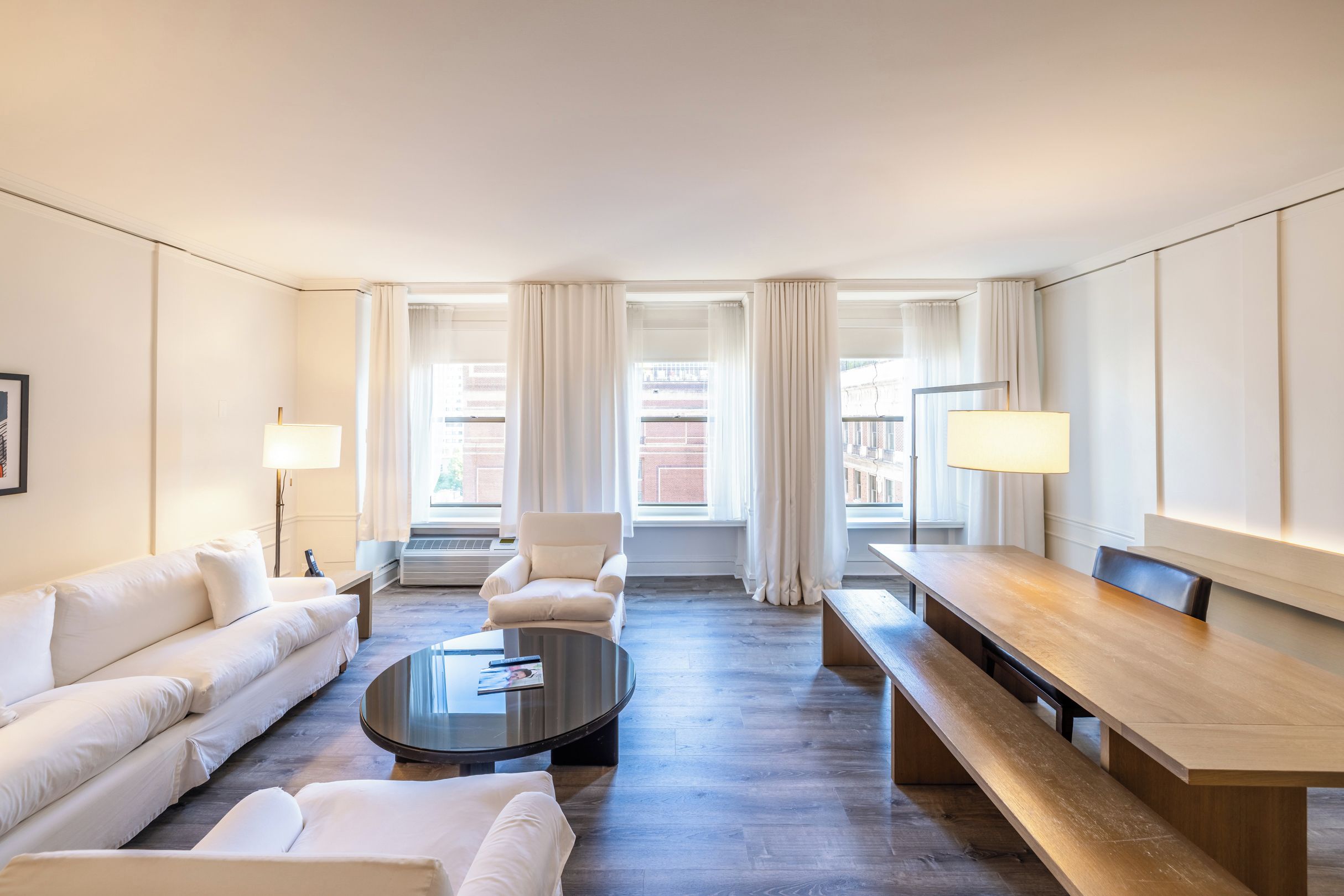 A hotel room with a sofa, a round coffee table, a dining table, and two lamps.