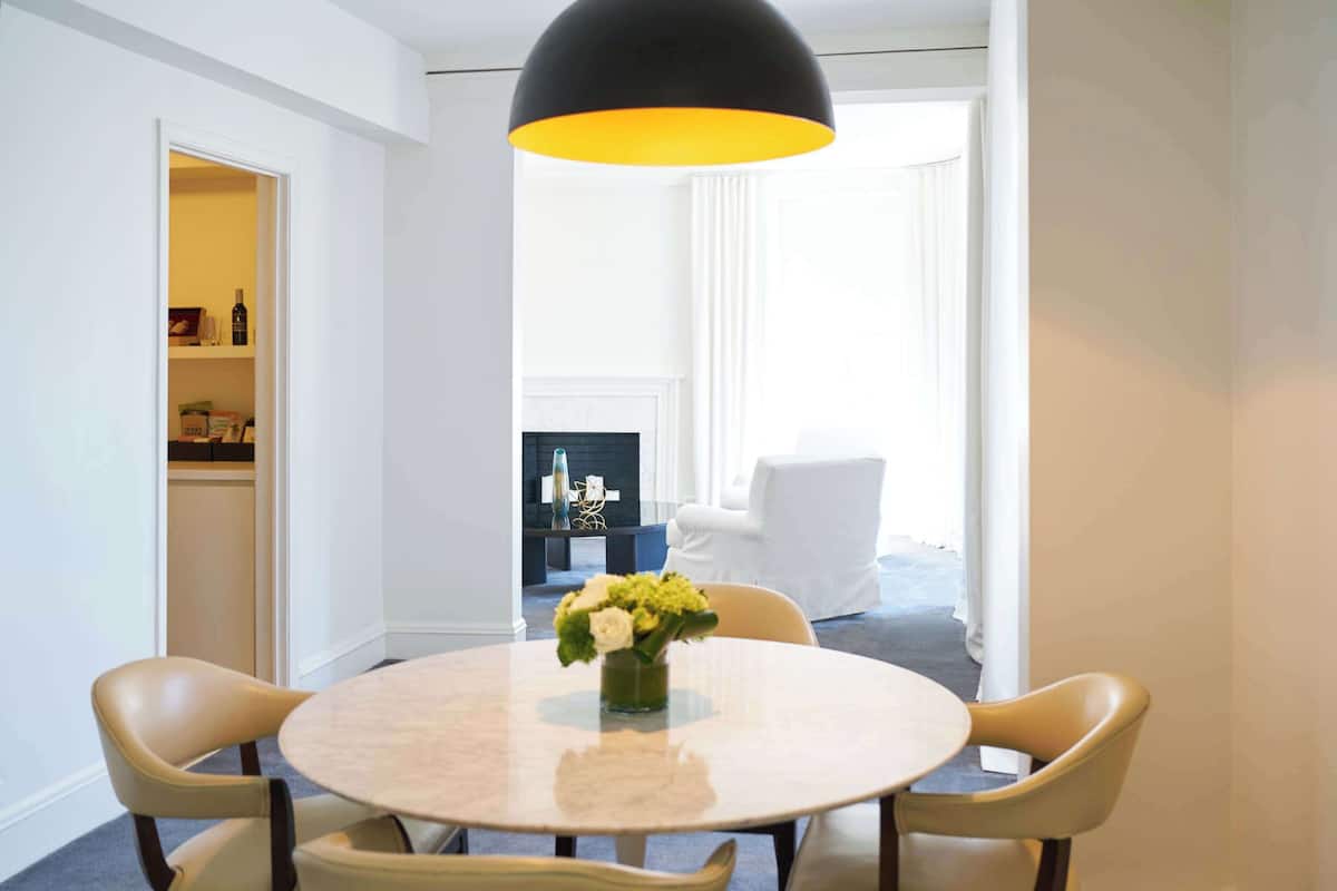 A modern dining area with a round table, four chairs, a vase of flowers, and a black pendant light.