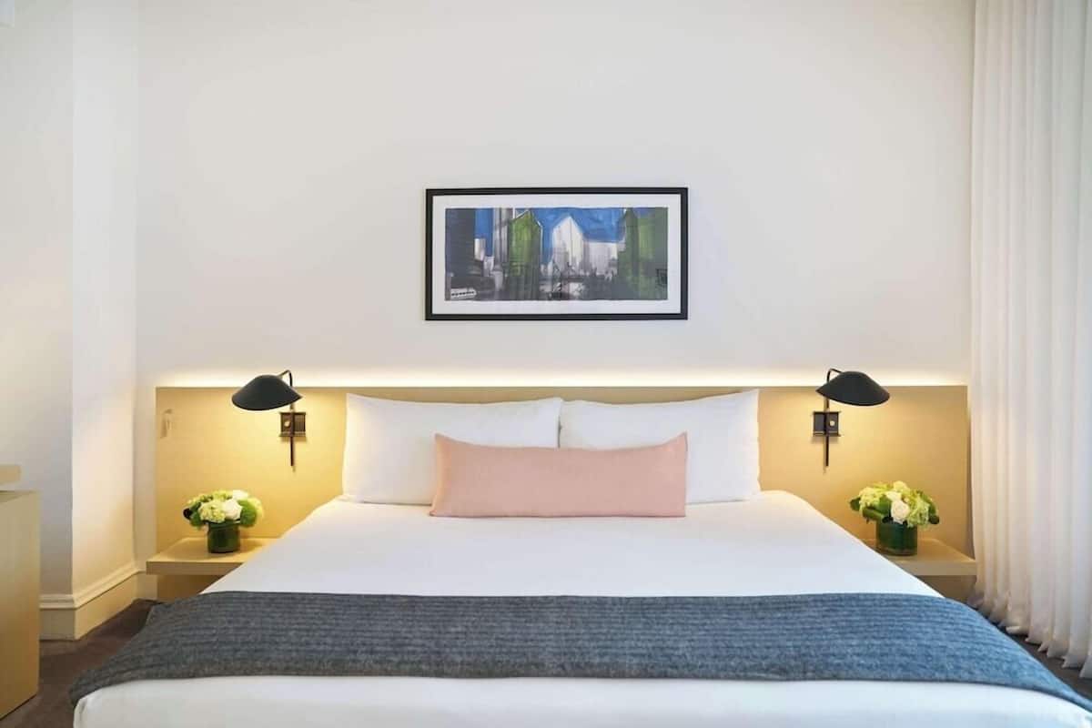 A hotel room with a large bed, two bedside tables with lamps, a framed picture on the wall, and a window with curtains.