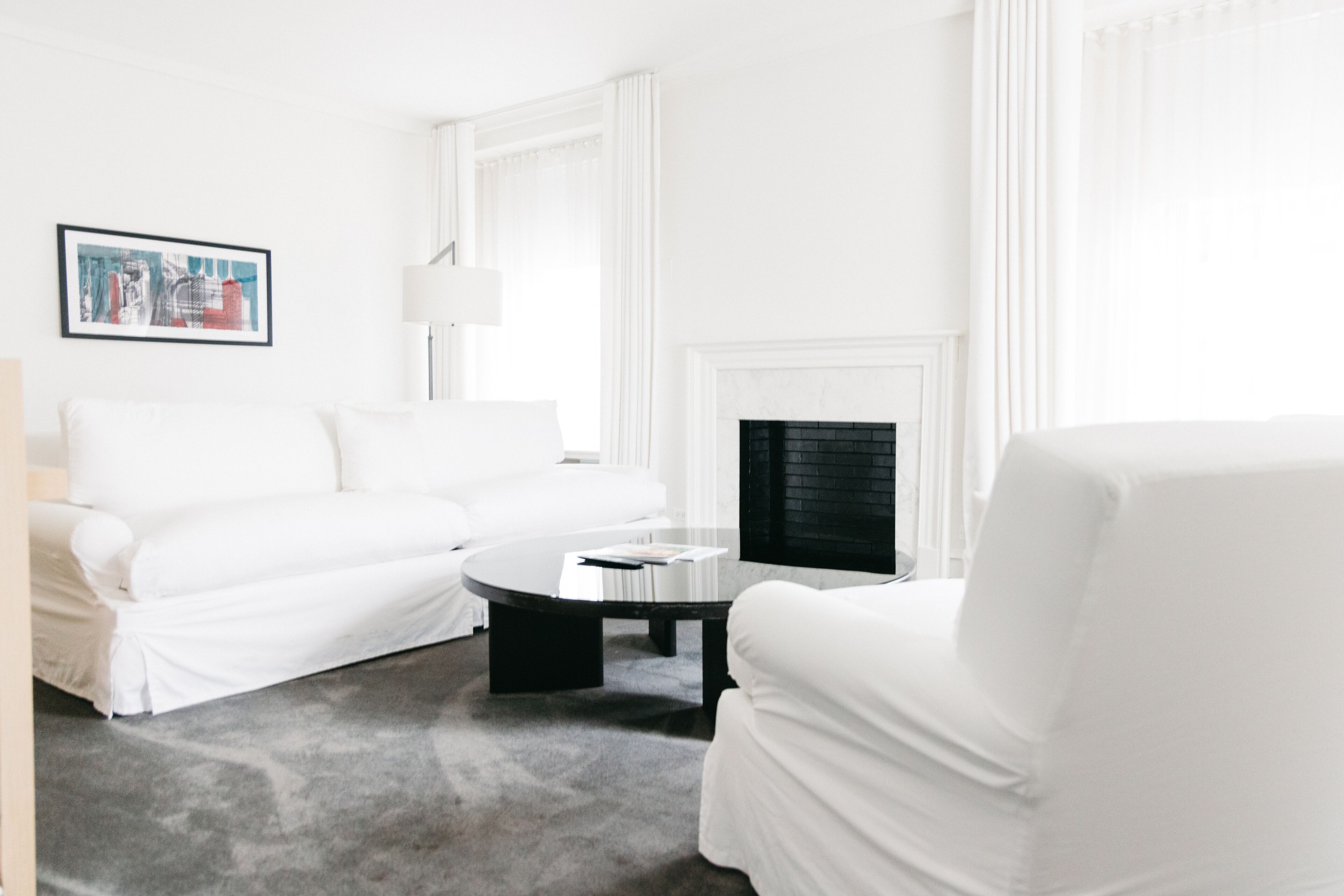 A modern, white-themed living room with a sofa, armchair, and a fireplace.