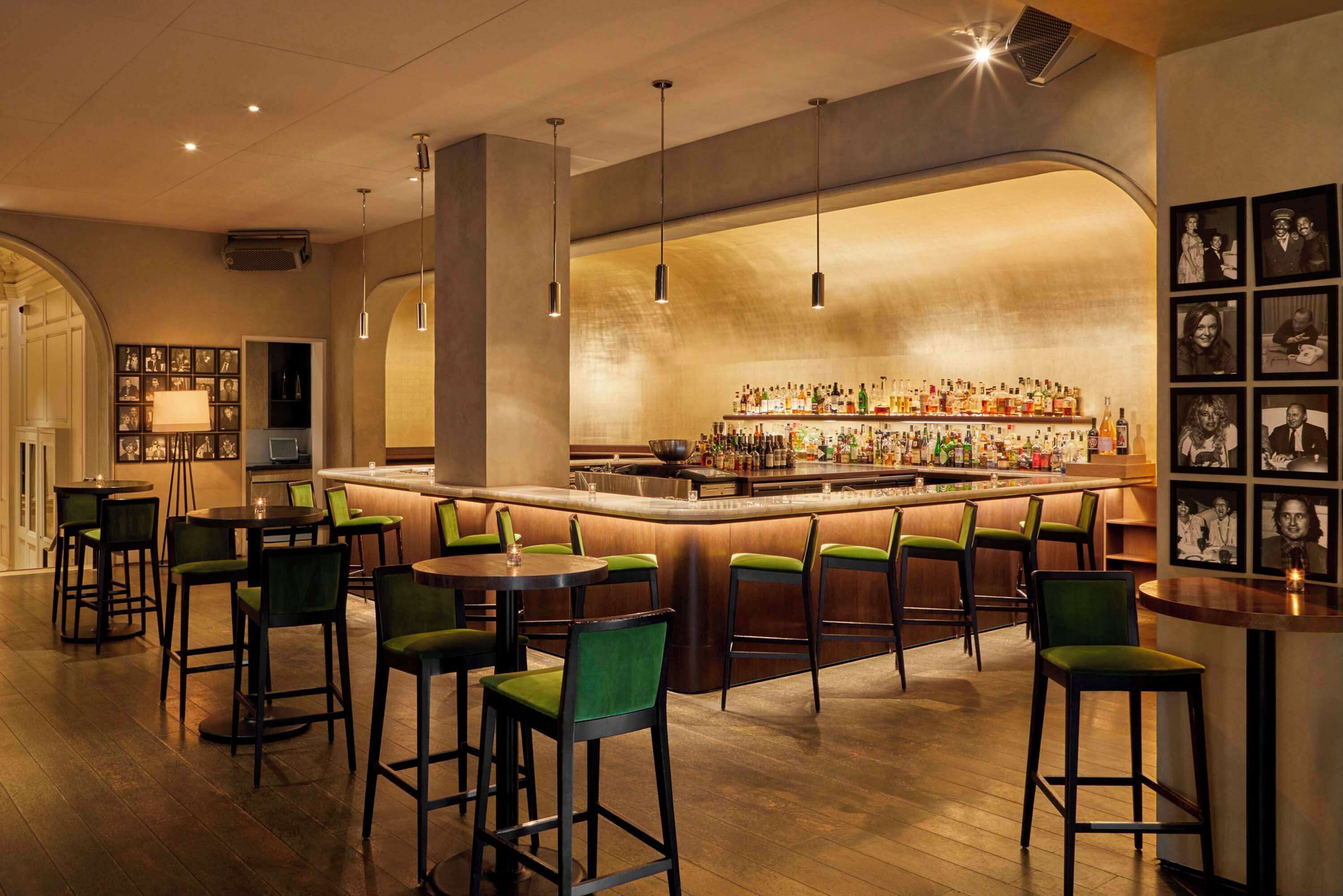 A bar area with a long counter, multiple bar stools, and a variety of bottles on shelves.