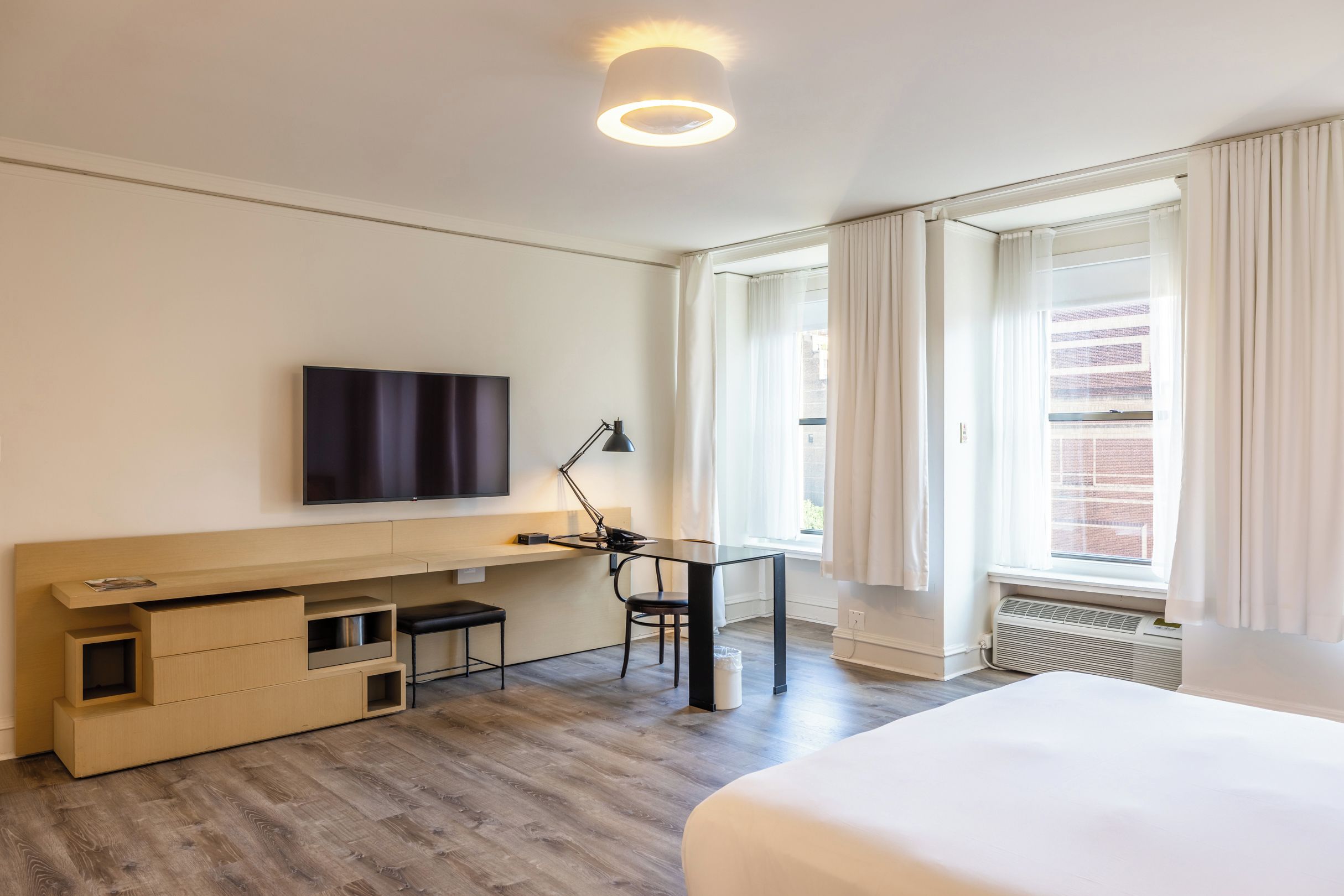 A hotel room with a bed, a desk with a chair, a television, and a window with curtains.
