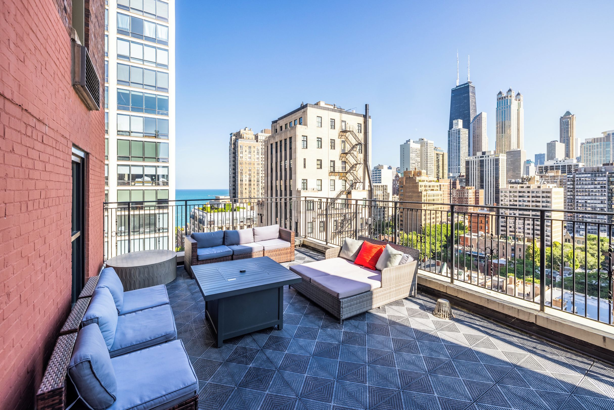 Terraço no telhado com área de estar ao ar livre, vista do horizonte da cidade e um edifício com fachada de tijolos.