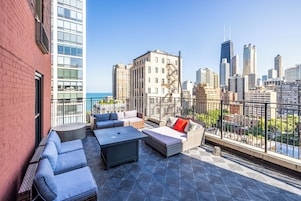 A rooftop terrace with outdoor seating, a view of the city skyline, and a building with a brick facade.