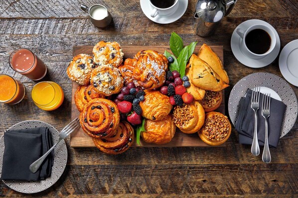 A breakfast spread with pastries, fruits, and beverages on a wooden table.