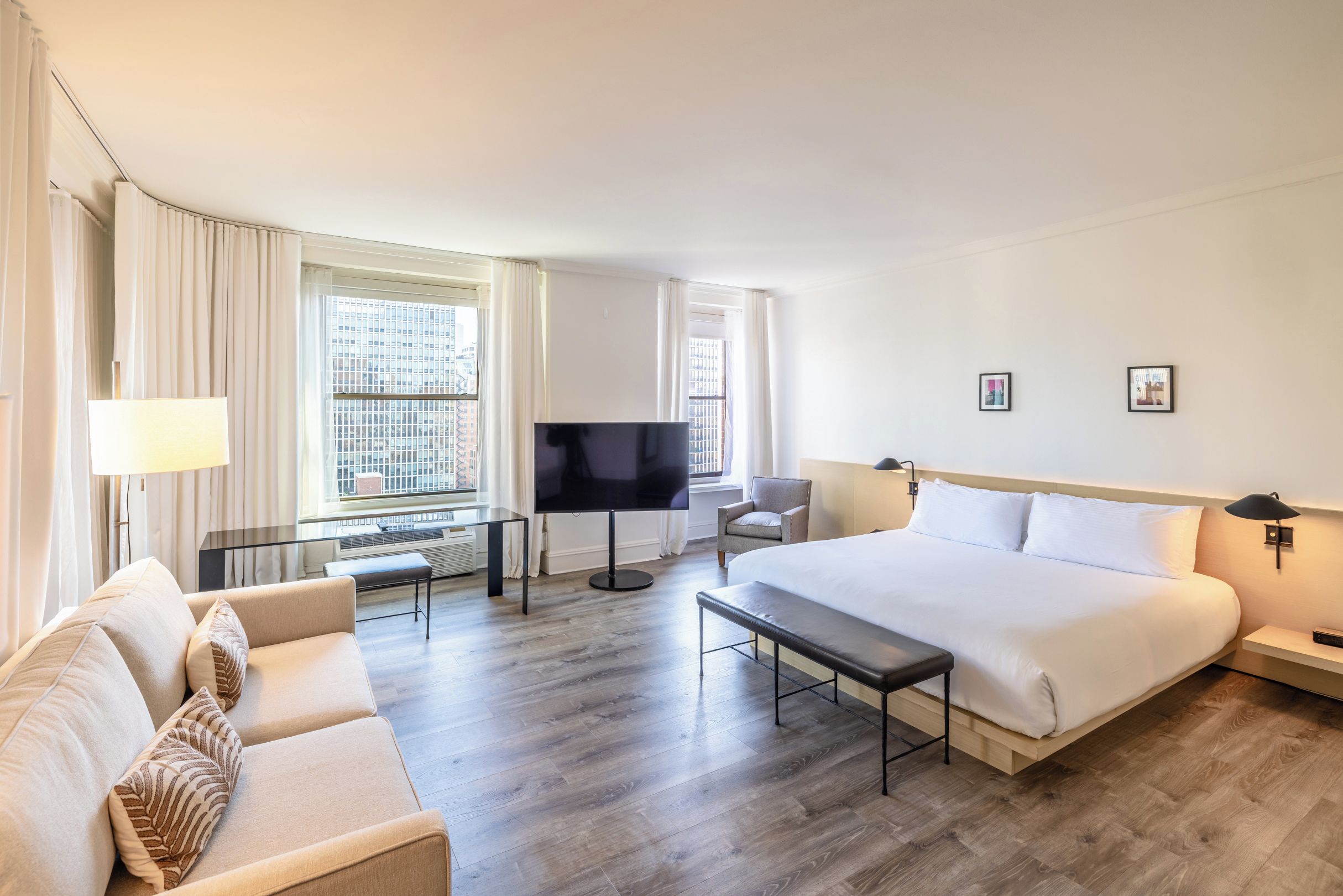 A hotel room with a bed, a sofa, a TV, a desk, and a chair.