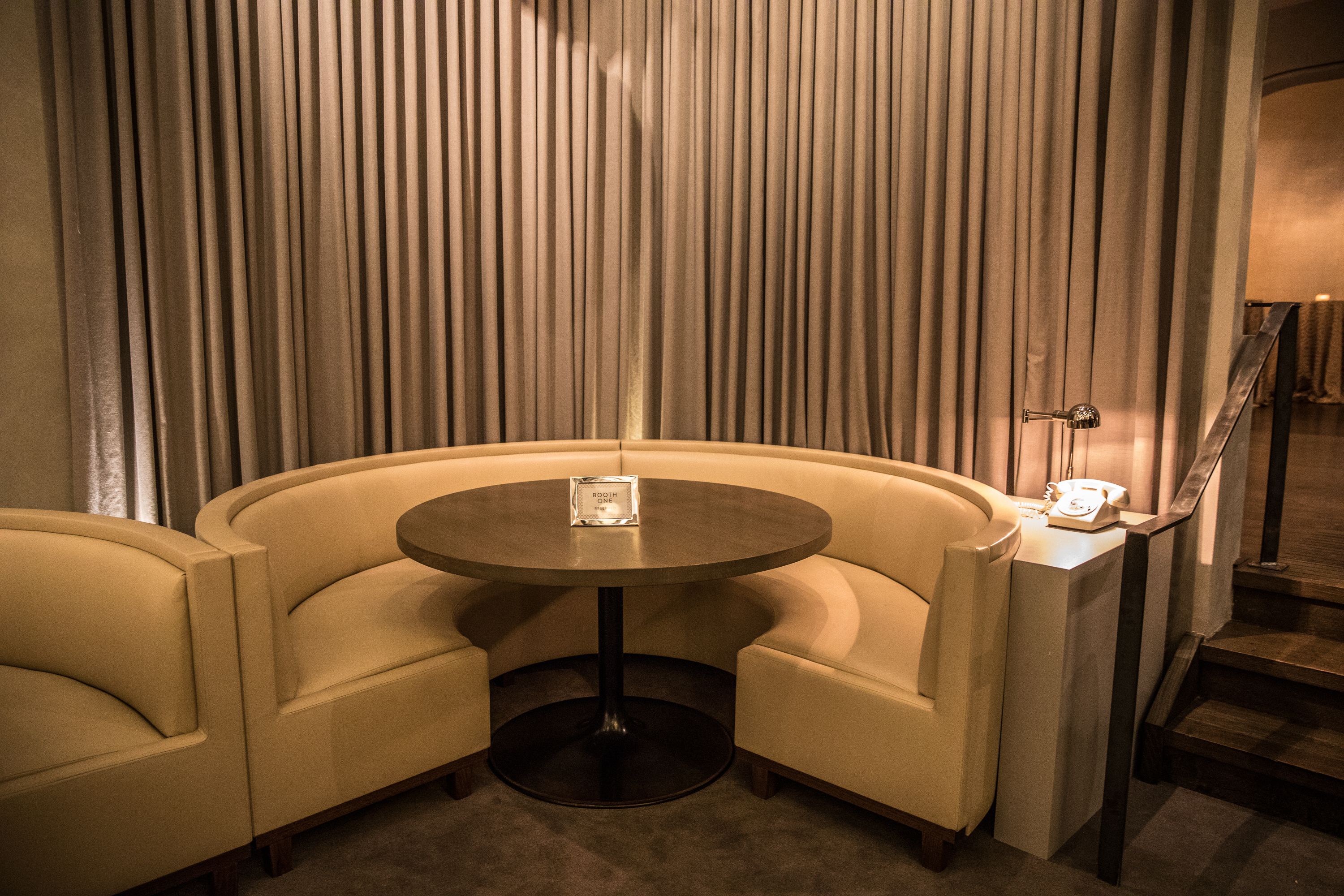 A corner seating area with a round table and two armchairs, a small table with a telephone, and a mirror on the wall.
