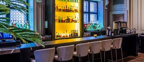 A bar area with a long counter, bar stools, and a display of bottles.