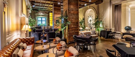 A spacious lounge area with leather sofas, round tables, and comfortable chairs, featuring a wooden ceiling and elegant decor.