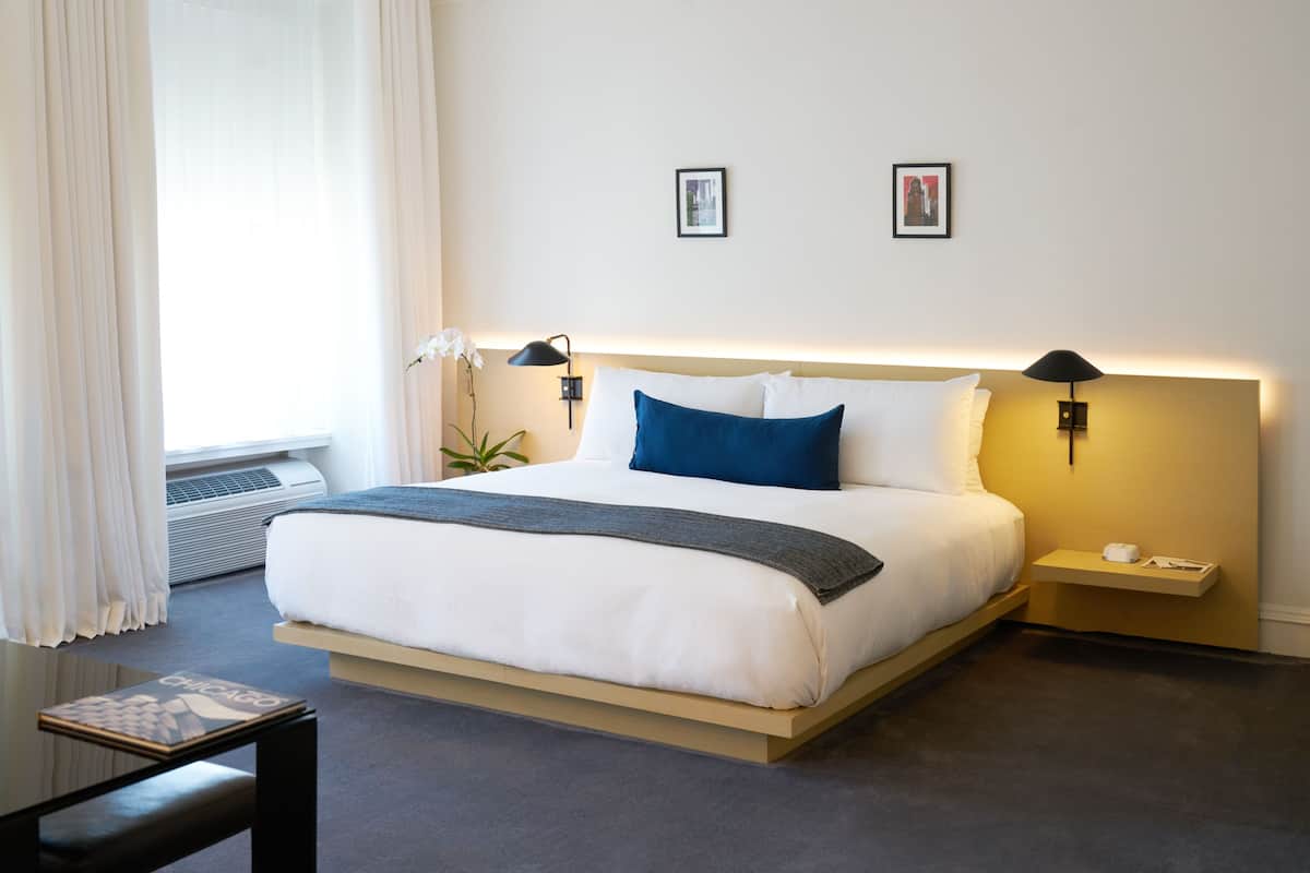 A neatly arranged hotel room with a large bed, bedside lamps, a small table, and a window with curtains.