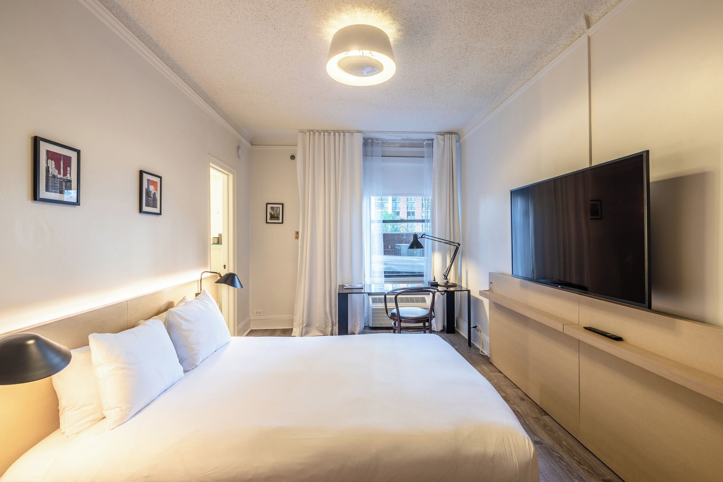 Een hotelkamer met een groot bed, een flatscreen televisie, een bureau met stoel en een raam met gordijnen.