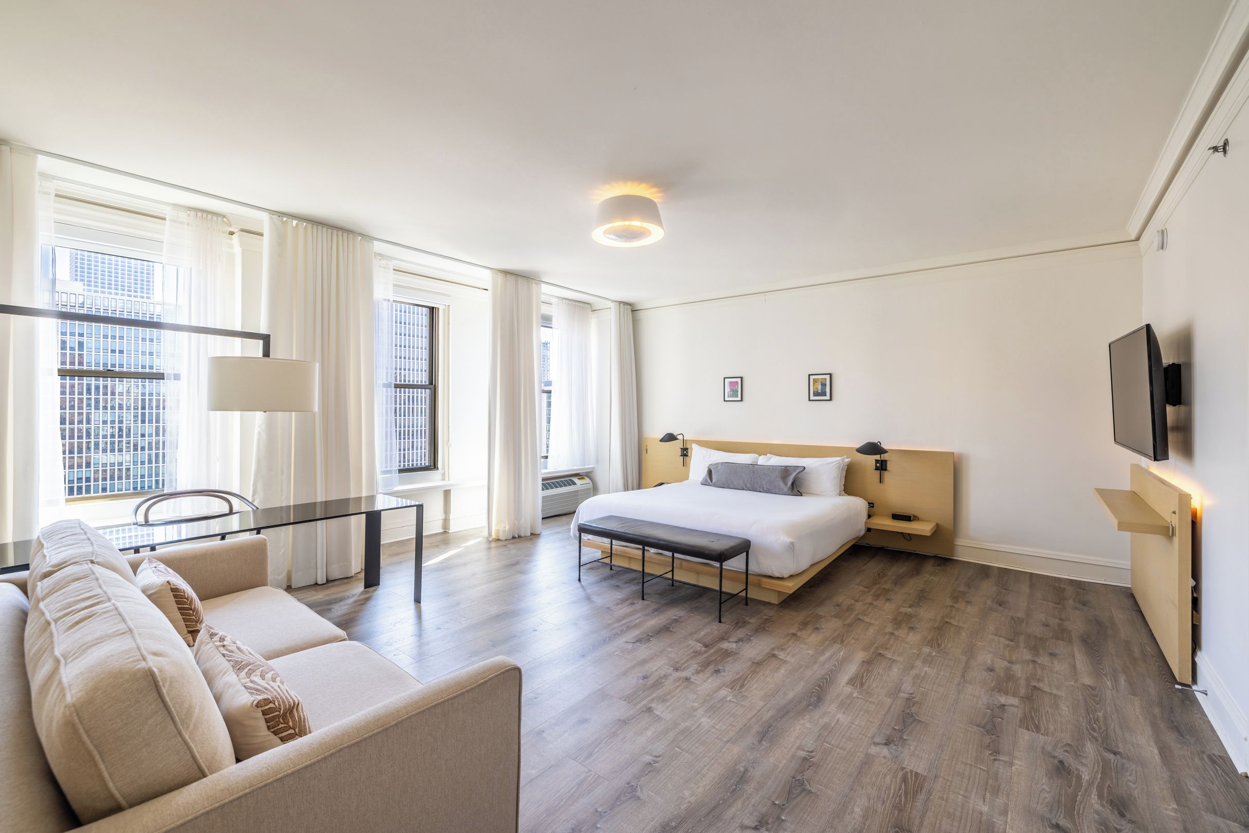 A hotel room with a bed, a desk, a sofa, and a TV.
