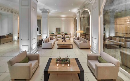 A spacious lobby with a central coffee table, sofas, and a large mirror.