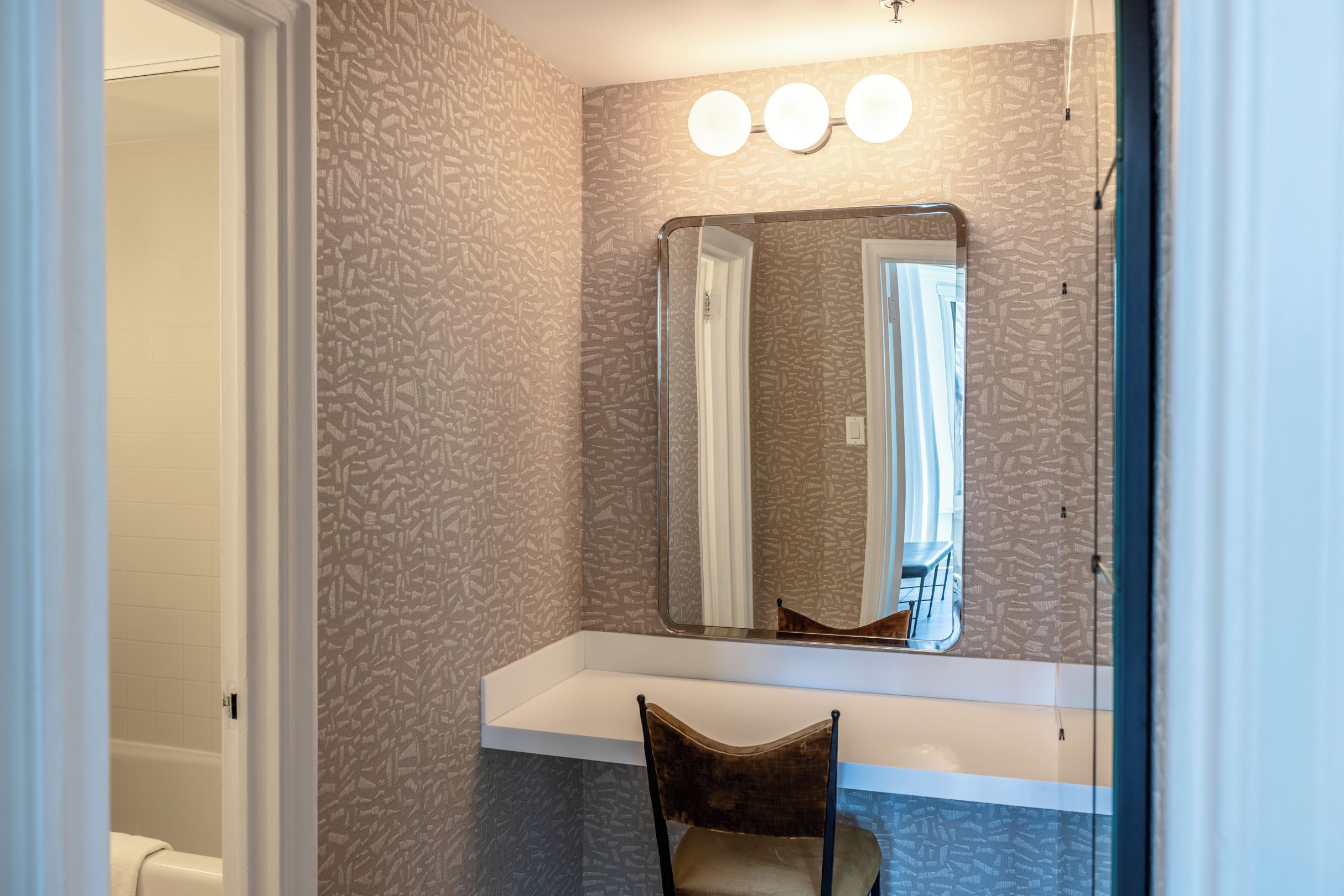 A bathroom with a vanity, a mirror, and a chair.